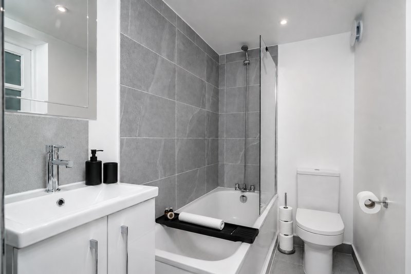 Modern bathroom with white vanity, gray tile walls, shower enclosure and toilet