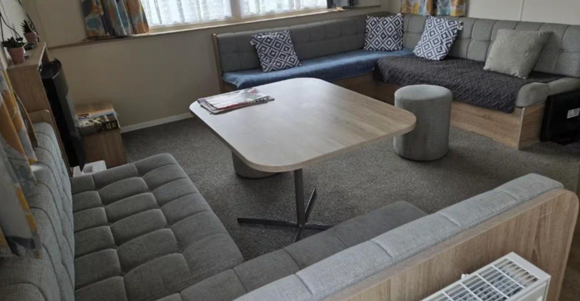 Open-plan living room with grey upholstered seating, wooden coffee table, and natural light from windows