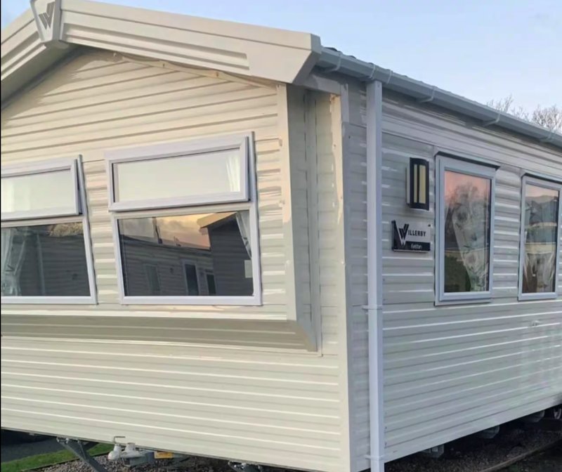 Exterior of cream and grey static caravan with large windows and entrance door