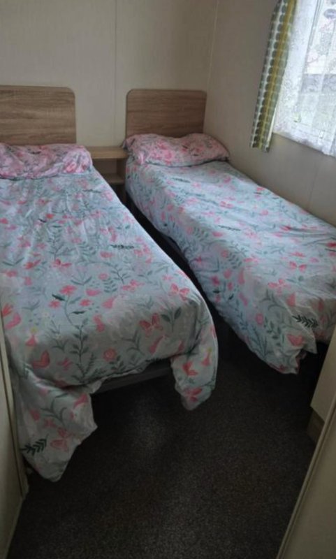 Twin bedroom with two single beds, wooden headboards, patterned bedding and window with curtains