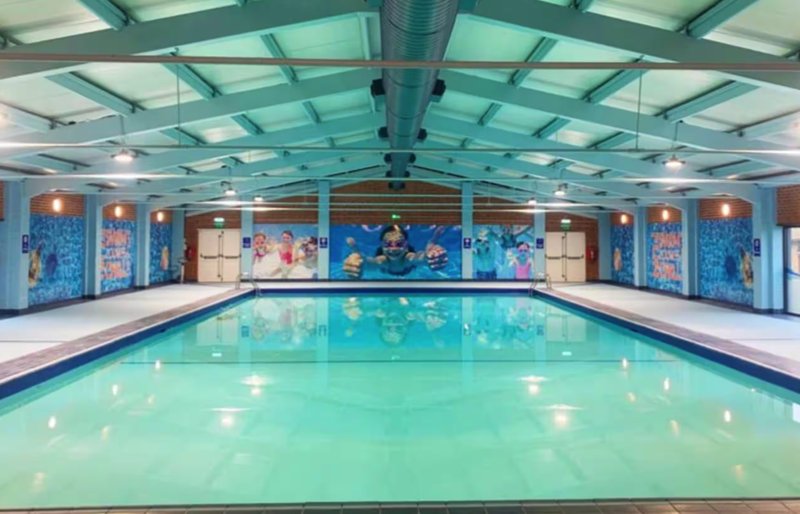 Indoor swimming pool with turquoise water, glass ceiling, and blue wall murals