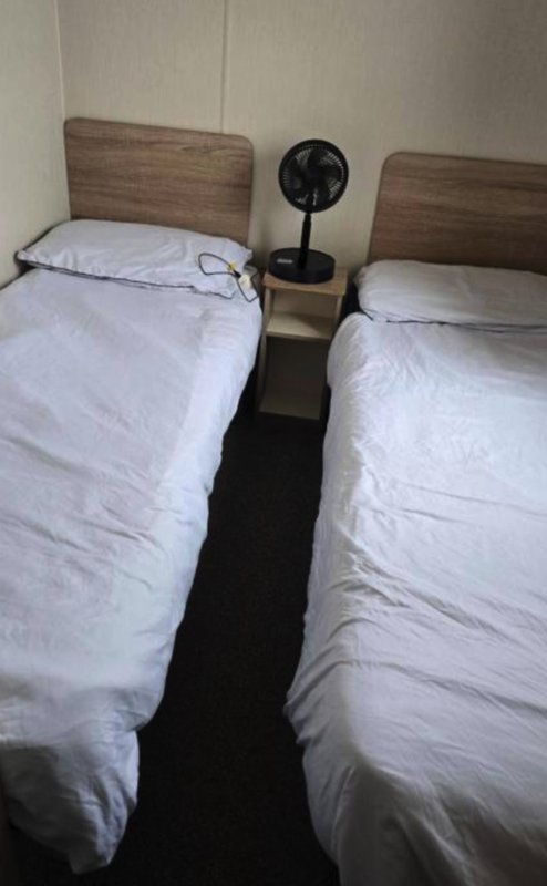 Twin bedroom with two single beds, white bedding, wooden headboards, and small fan between beds