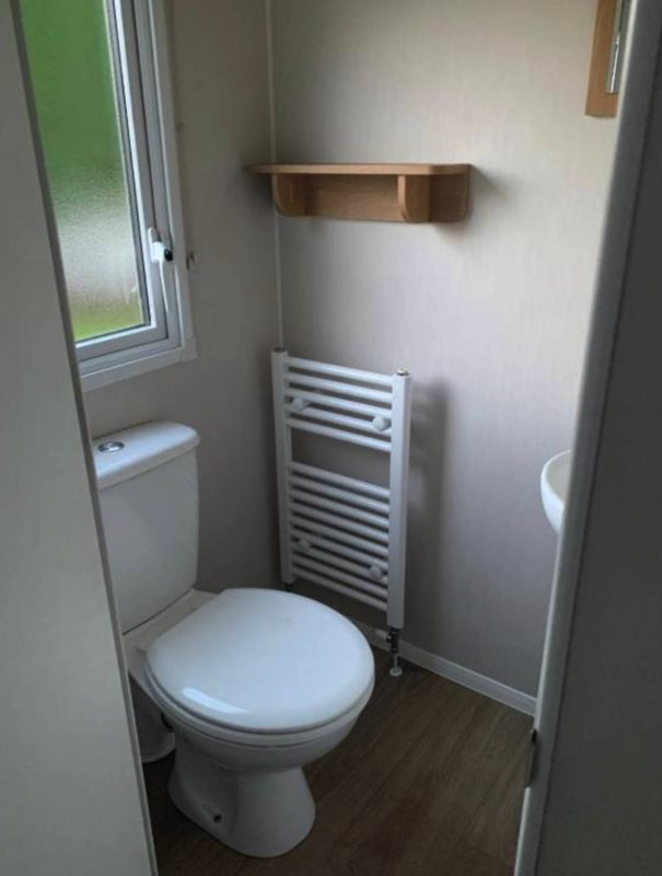 Compact bathroom with toilet, heated towel rail, wooden shelf and frosted window