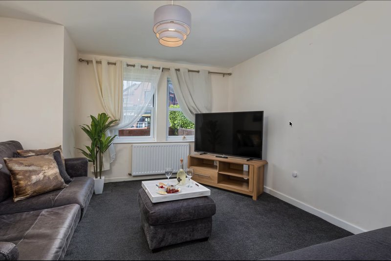 Living room with grey sofa, TV on wooden stand, dark carpet and window with curtains