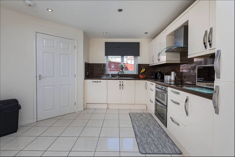 Modern kitchen with white cabinetry, black splashback, tiled floor and integrated appliances