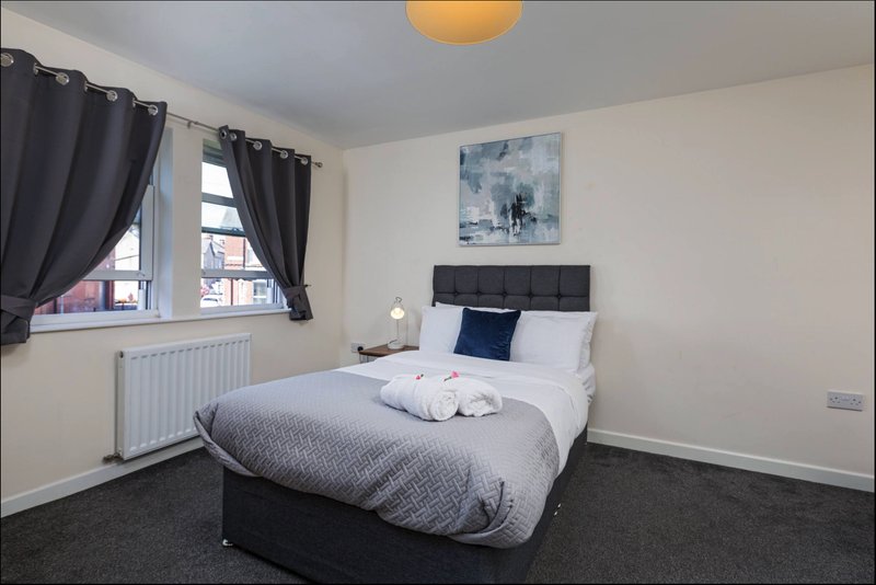 Bedroom with double bed, dark headboard, grey bedding, black curtains, and window with street view