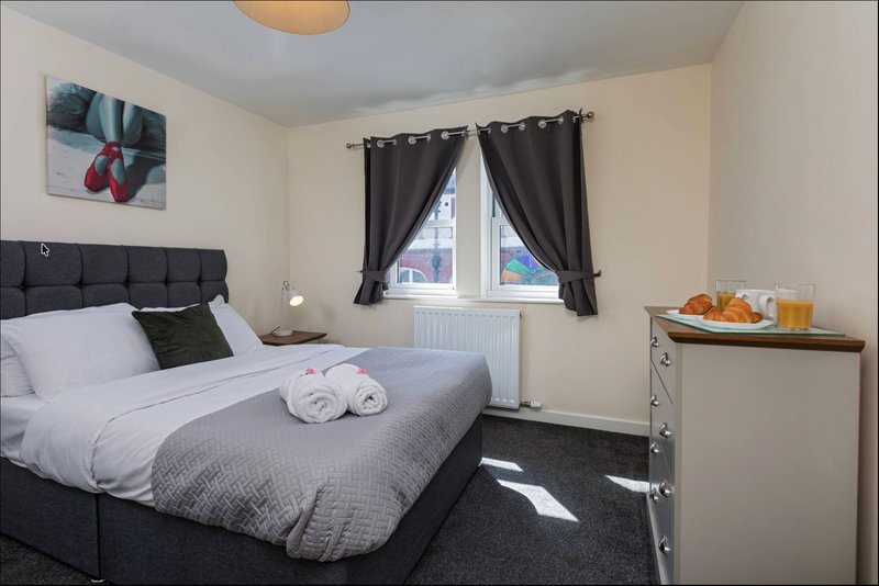Bedroom with double bed, dark headboard, window with black curtains, and bedside table with lamp