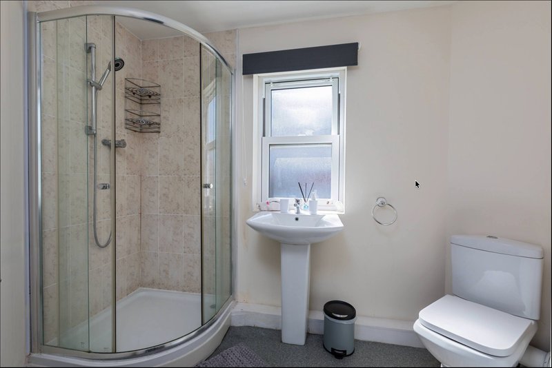 Modern bathroom with curved glass shower enclosure, pedestal sink, toilet and window