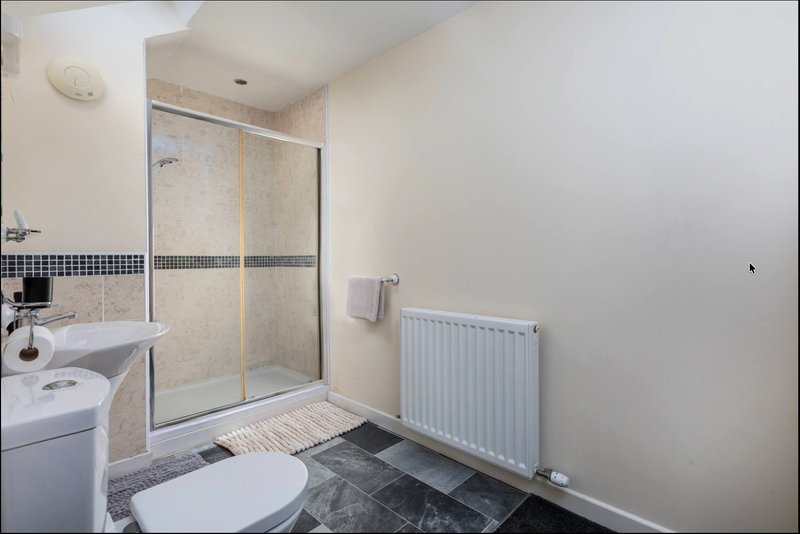 Modern bathroom with shower enclosure, toilet, sink, radiator and tiled flooring