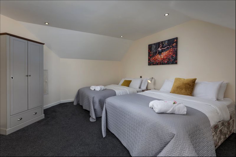 Bedroom with two double beds, white bedding, gold cushions, wardrobe and wall art