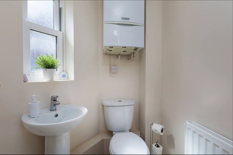 Clean bathroom with pedestal sink, toilet, window, and wall-mounted boiler