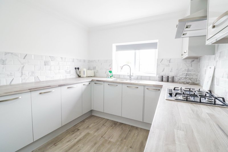 Modern kitchen with white cabinetry, marble backsplash, gas hob and wooden floor