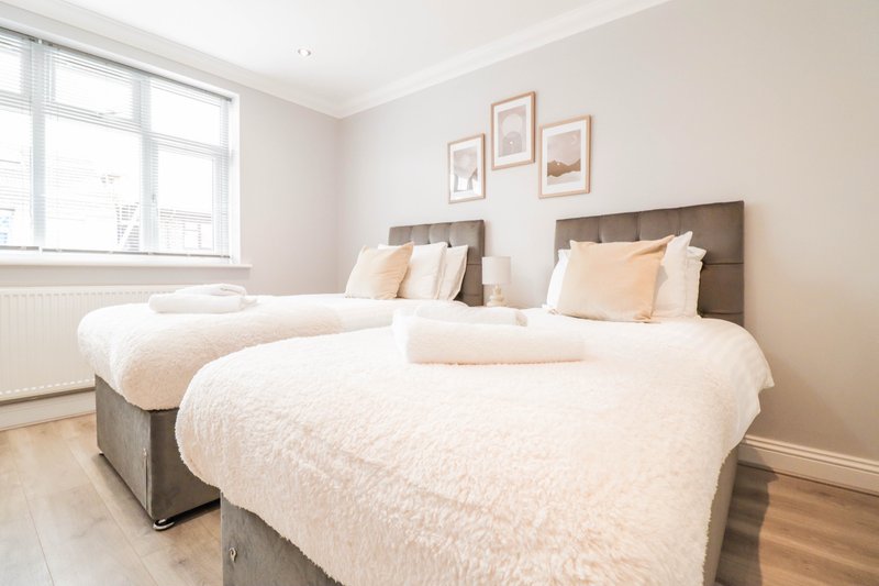 Bright bedroom with two double beds, cream bedding, framed wall art, and large window