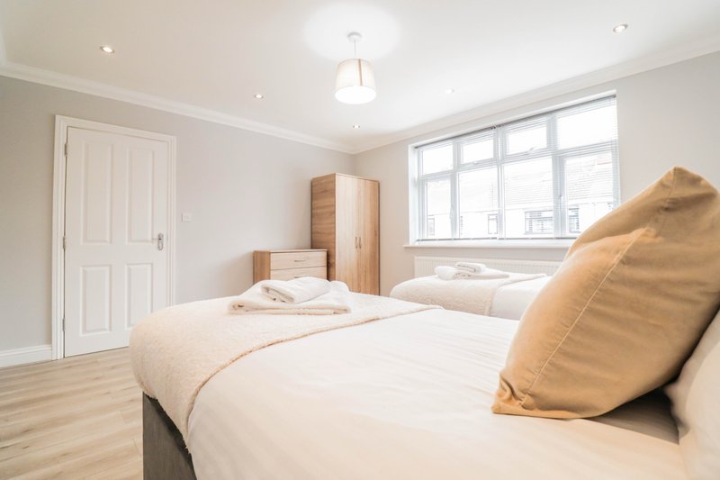Modern bedroom with two single beds, wooden wardrobes, large window and light wood flooring