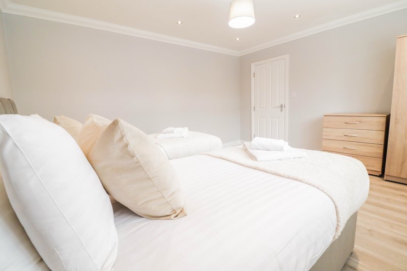 Bright bedroom with white bedding, cream pillows, wooden dresser and light wood flooring