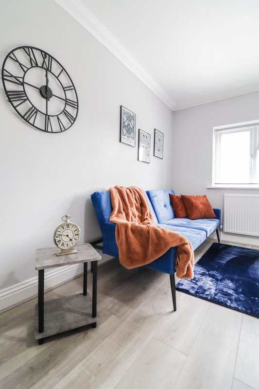 Bright modern living room with blue sofa, orange throw blanket, wall clock, small side table and window