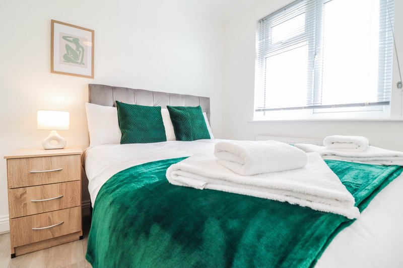 Bedroom with double bed, green bedding, white pillows, wooden nightstand and lamp