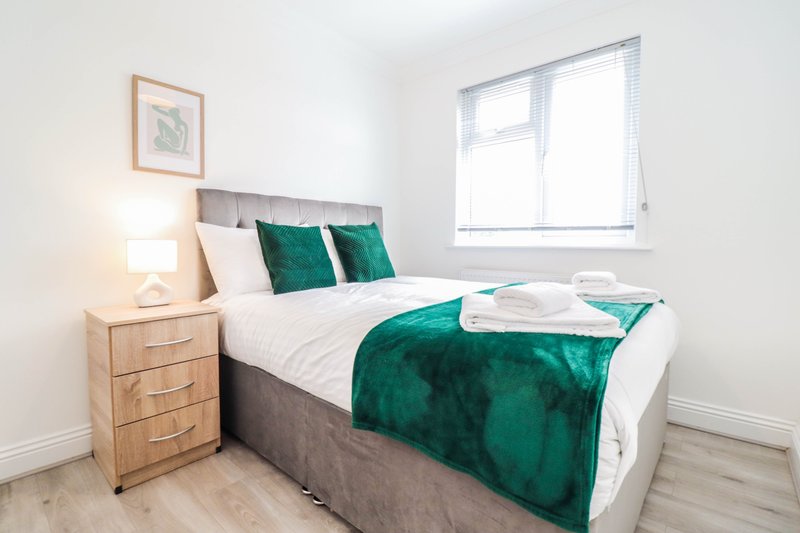 Bright bedroom with double bed, green velvet throw, wooden nightstand and bedside lamp