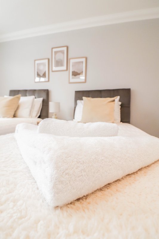 Bright bedroom with two single beds, cream bedding, and framed wall art above headboards
