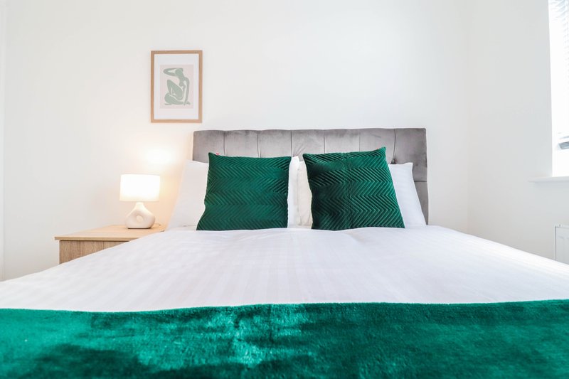 Modern bedroom with double bed, green cushions, white bedding and wooden nightstand