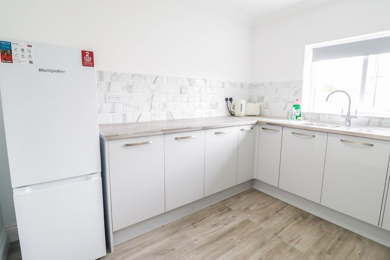 Modern kitchen with white cabinets, marble backsplash, wooden floor and stainless steel sink