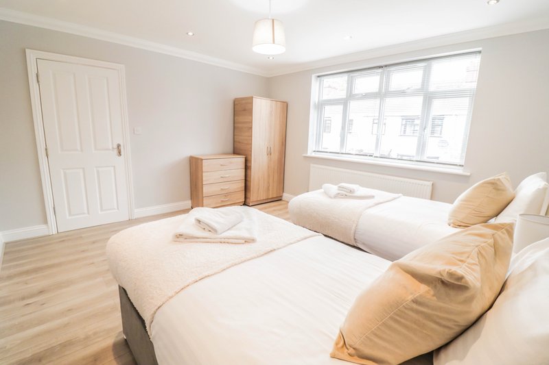 Bright bedroom with two single beds, wooden furniture, and large window overlooking street