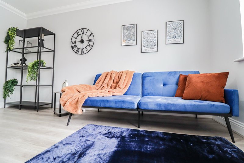 Modern living room with blue sofa, orange throw blanket, potted plants and wall clock