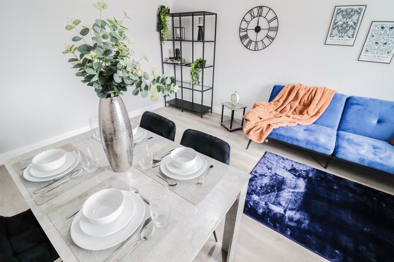 Modern dining area with set table, fresh flowers, wall clock, and blue sofa in background