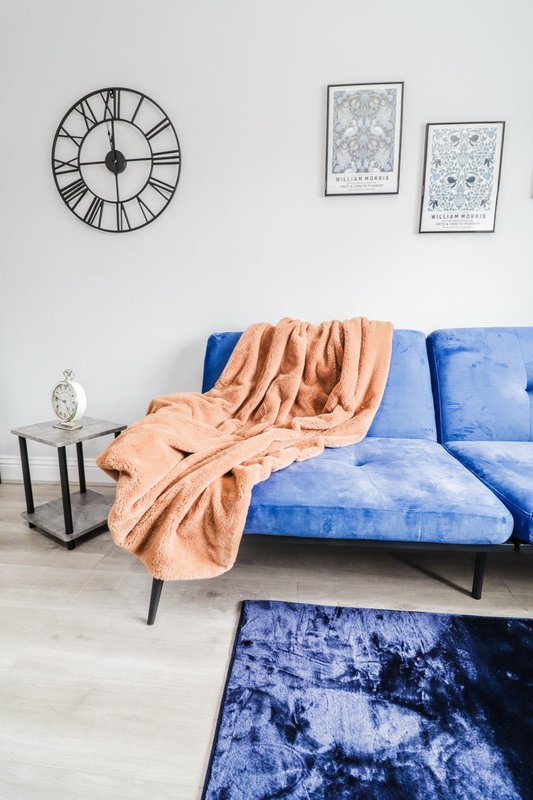 Living room with blue velvet sofa, peach throw blanket, wall clock and framed artwork