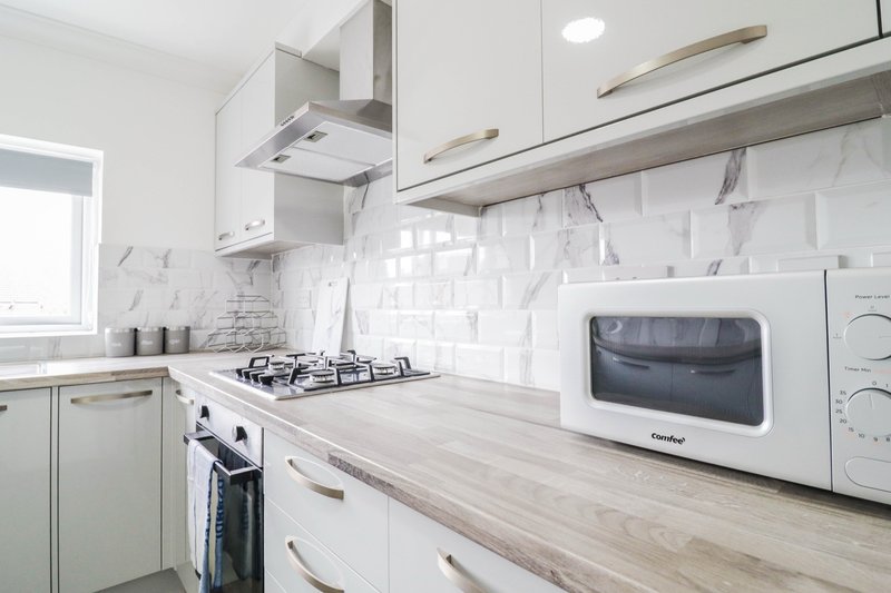 Modern kitchen with white cabinetry, marble backsplash, gas stovetop and white microwave