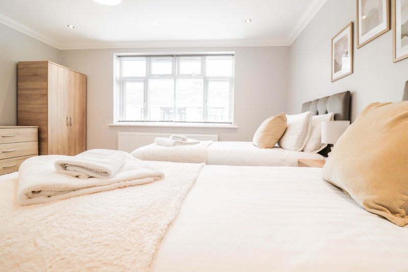 Bright bedroom with two single beds, wooden wardrobe, large window and neutral furnishings