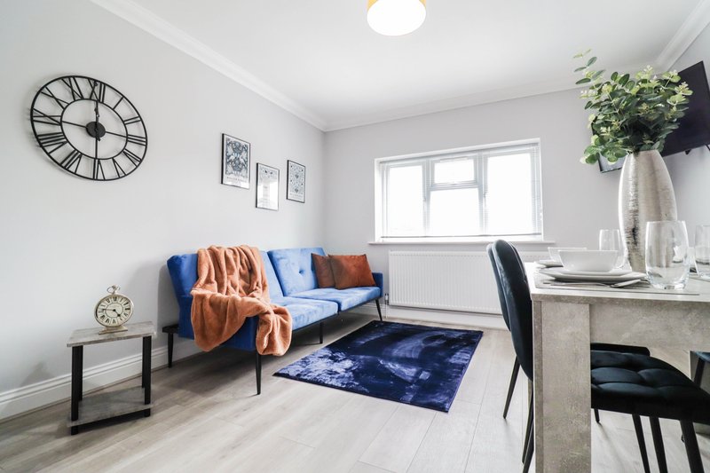 Bright living room with blue sofa, wooden floor, wall clock and desk area