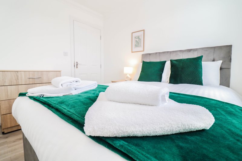 Bedroom with double bed, green bedding, white pillows and towels, wooden furniture