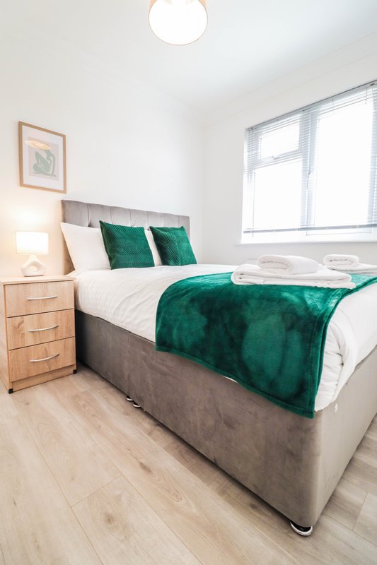 Bright bedroom with double bed, green velvet bedding, wooden nightstand and window