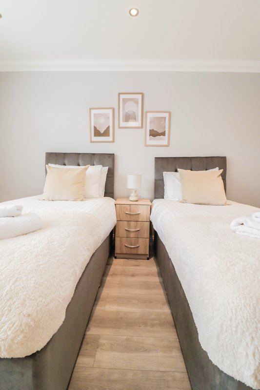 Twin bedroom with two single beds, wooden nightstand, framed wall art, and wooden flooring