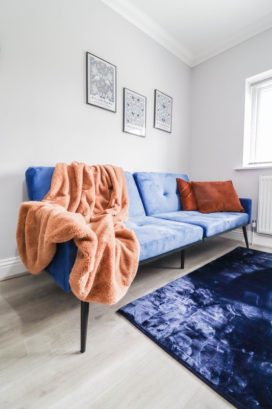 Modern living room with blue sofa, orange throw blankets, framed wall art, and dark blue rug