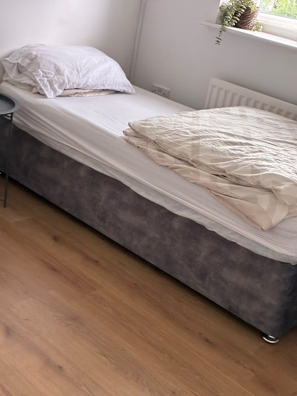 Bedroom with single bed, white pillow, rumpled bedding, wooden floor and radiator