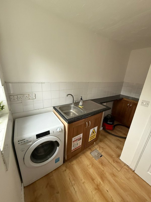 Utility room with washing machine, sink, and wooden cabinetry on laminate flooring