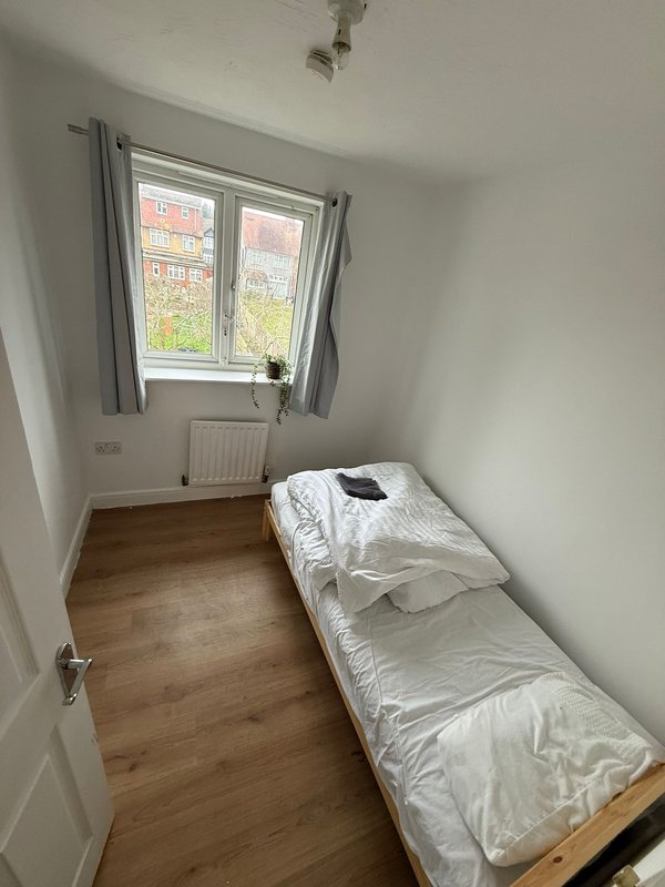 Small bedroom with single bed, wooden floor, window with grey curtains and radiator