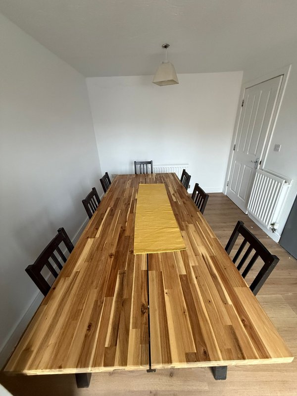 Spacious dining room with long wooden table, black chairs, yellow runner, and pendant light