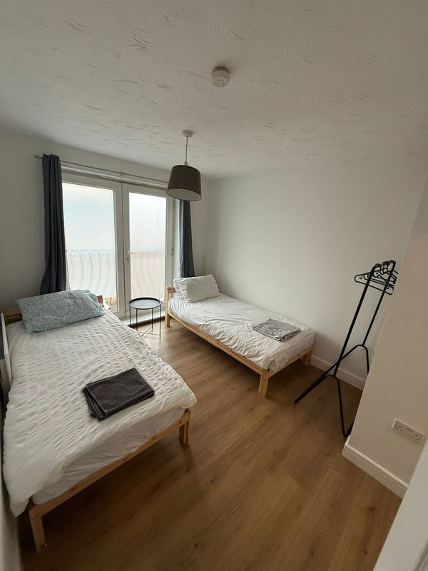 Bedroom with two single beds, wooden floor, pendant light, and glass balcony doors