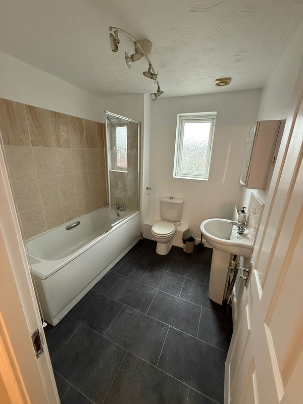 Clean bathroom with bathtub, toilet, sink, dark tile flooring and window
