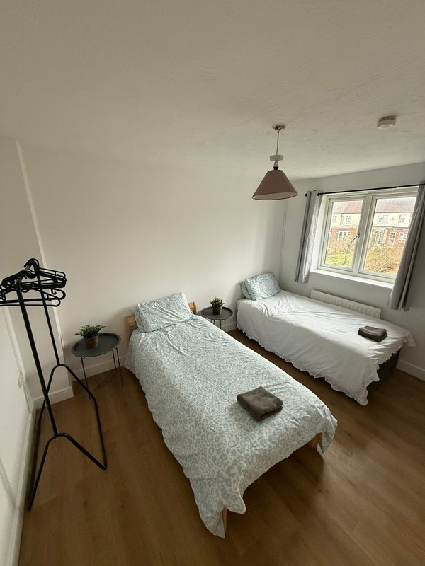 Bright bedroom with two single beds, pendant light, wooden floor and large window