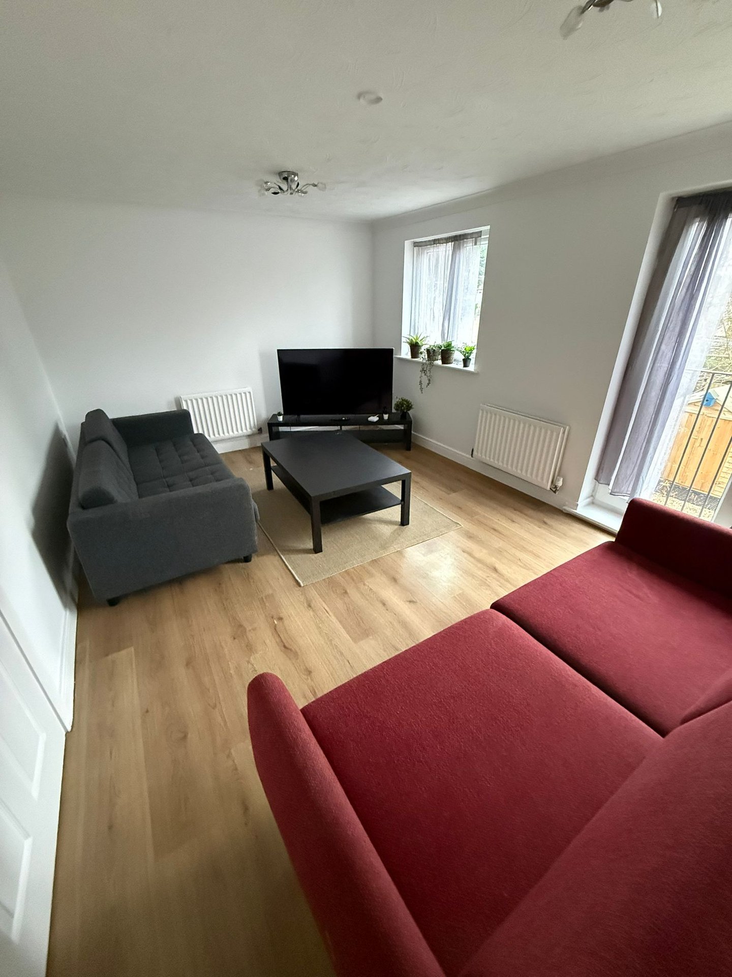 Bright living room with red and grey sofas, wooden floor, TV stand and dual windows