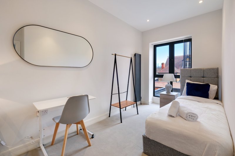 Modern bedroom with single bed, desk, chair, oval mirror and city view through window