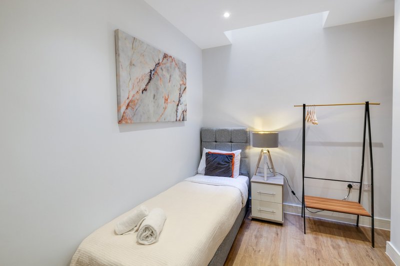 Modern bedroom with single bed, grey headboard, wooden floor and skylight window