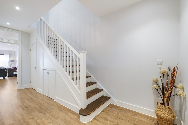 Modern hallway with wooden staircase, white railings, and dried flower arrangement