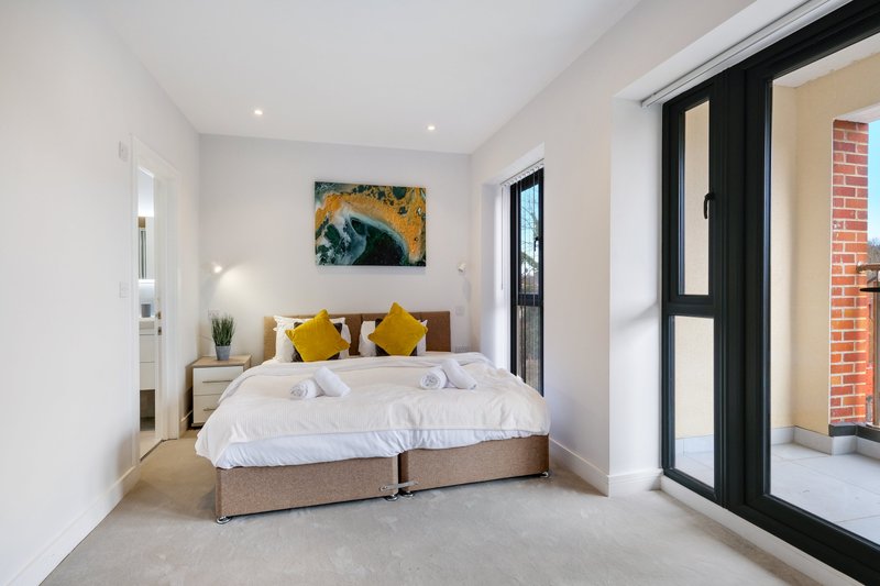Modern bedroom with double bed, yellow cushions, artwork, and glass door to garden