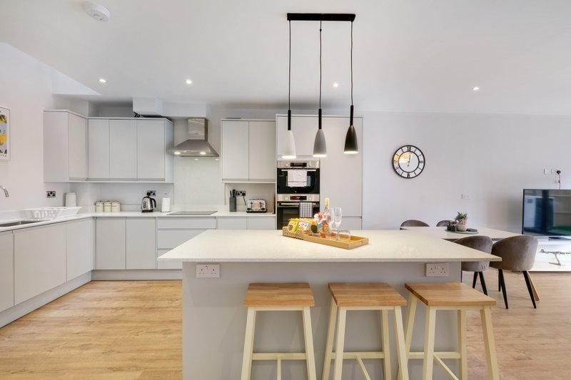 Modern white kitchen with island, pendant lights, wooden flooring and dining area
