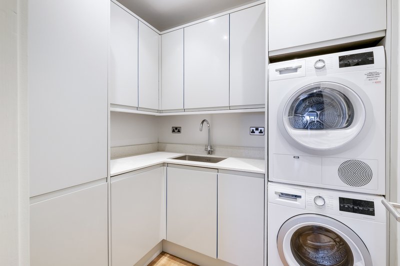 Modern laundry room with stacked white washing machine and dryer, white cabinetry and sink